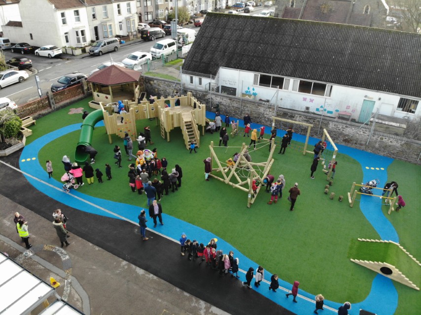 A school playground that has artificial grass flooring and a variety of pieces of active playground equipment on top.