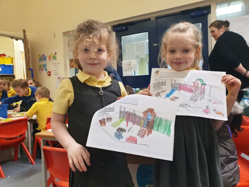 Two girls are holding up their playground designs to the camera and smiling.