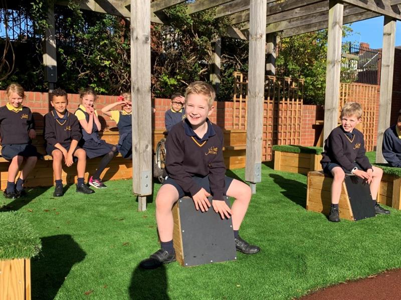 Two children sat on drum seats placed onto artificial grass surfacing