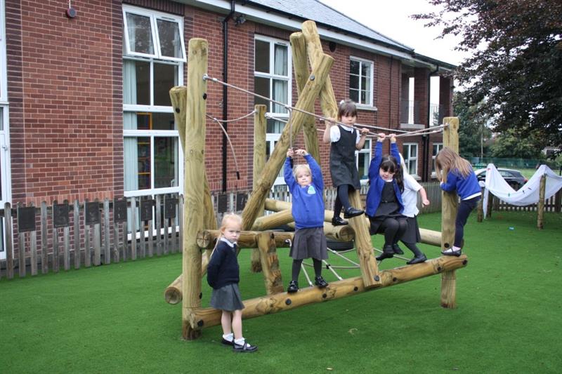 children in school uniform climb and swing on the climbing frame on artificial grass surfacing