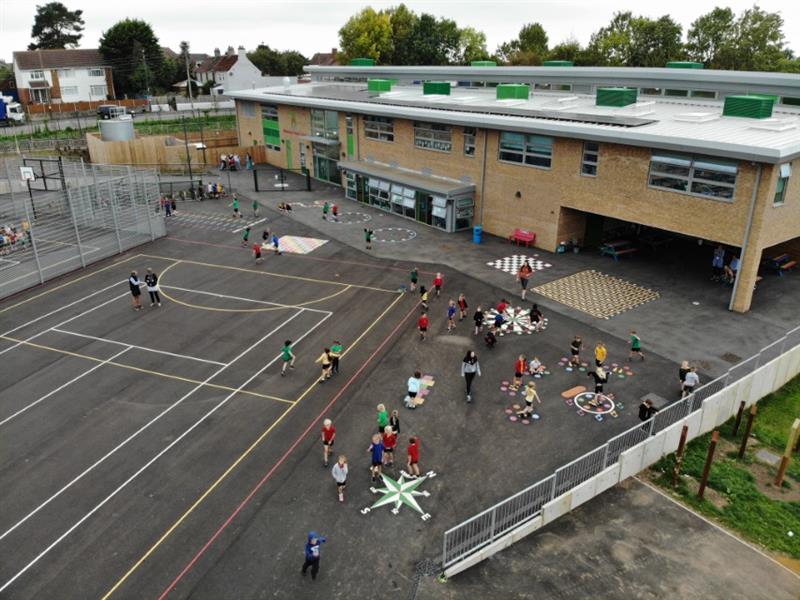 Aerial view of large playground with lots of different playground markings on including a white and green compass, all the markings have been installed in front of the school building. 