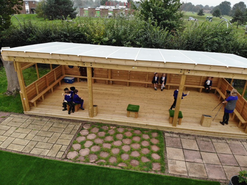 Small groups of children are sat inside an outdoor classroom, each sitting in a different part.