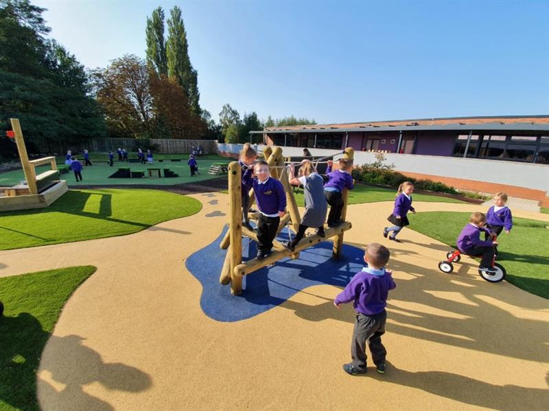 Several children in a purple school uniform play on beige and blue wetpour on a timber playframe