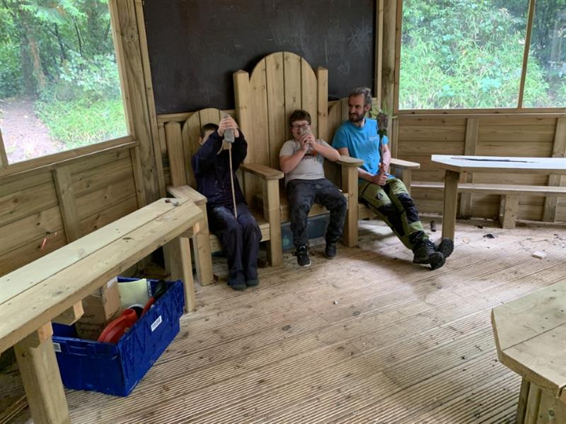 two children and one adult are sat on our story telling chair in an outdoor classroom 