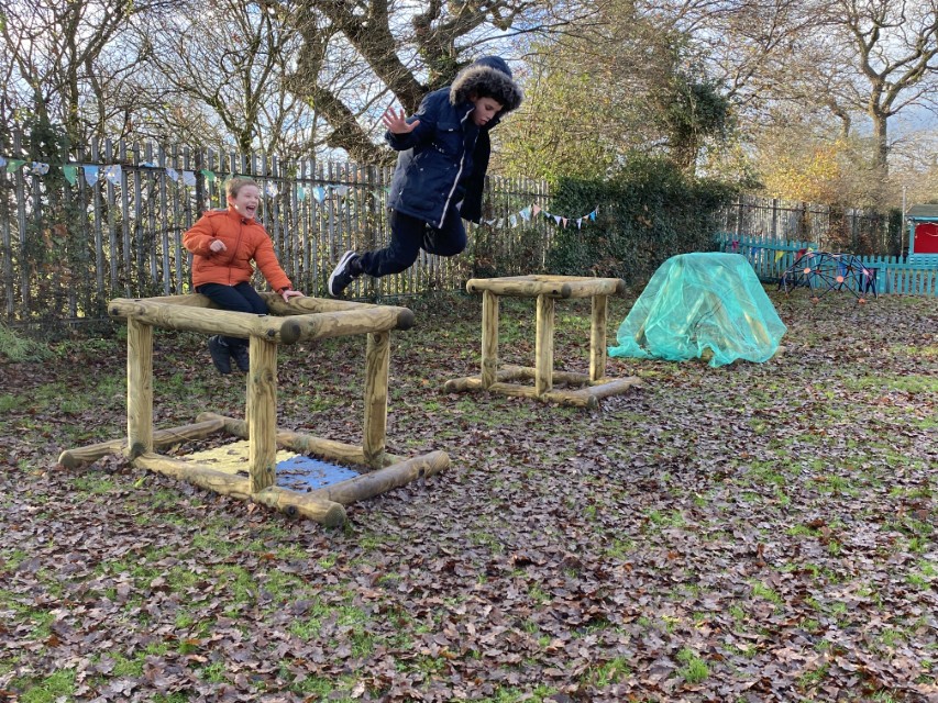 Two SEN boys are playing in nature and are jumping off play equipment.