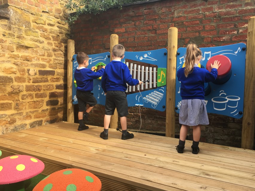 Three children are playing with outdoor musical instruments that have been attached to a performance stage.