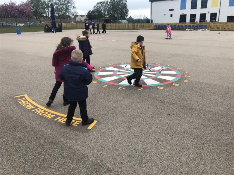 Children playing outside on playground darts on school playground using a darts playground markings feature to throw darts and add up their scores. 