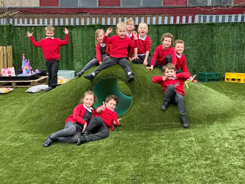 children in red, black and white school uniform sit on top of the crawl through tunnel hill and smile at the camera as they pose for a picture