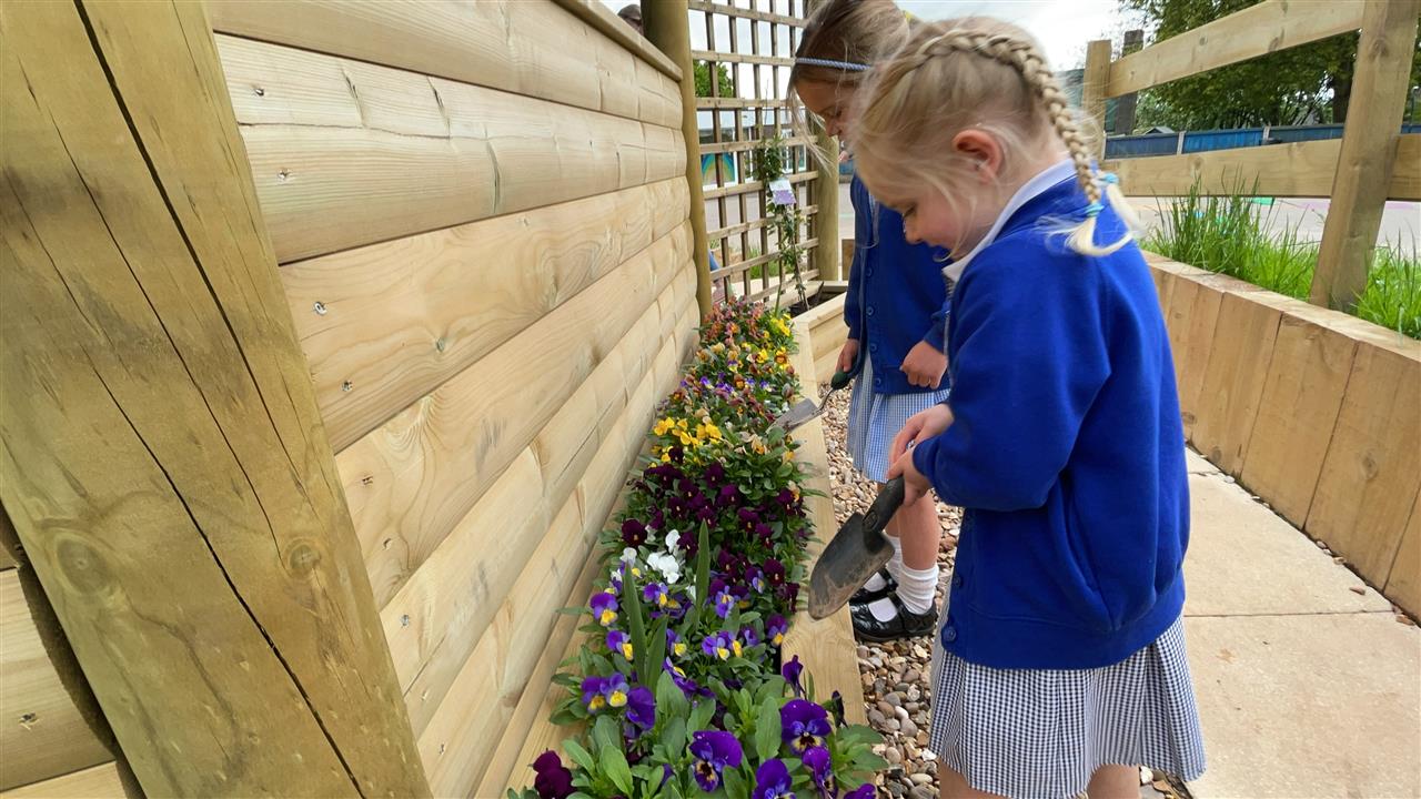 Two little girls are watering the flowers that surround the outdoor classroom. The children look happy and joyful.