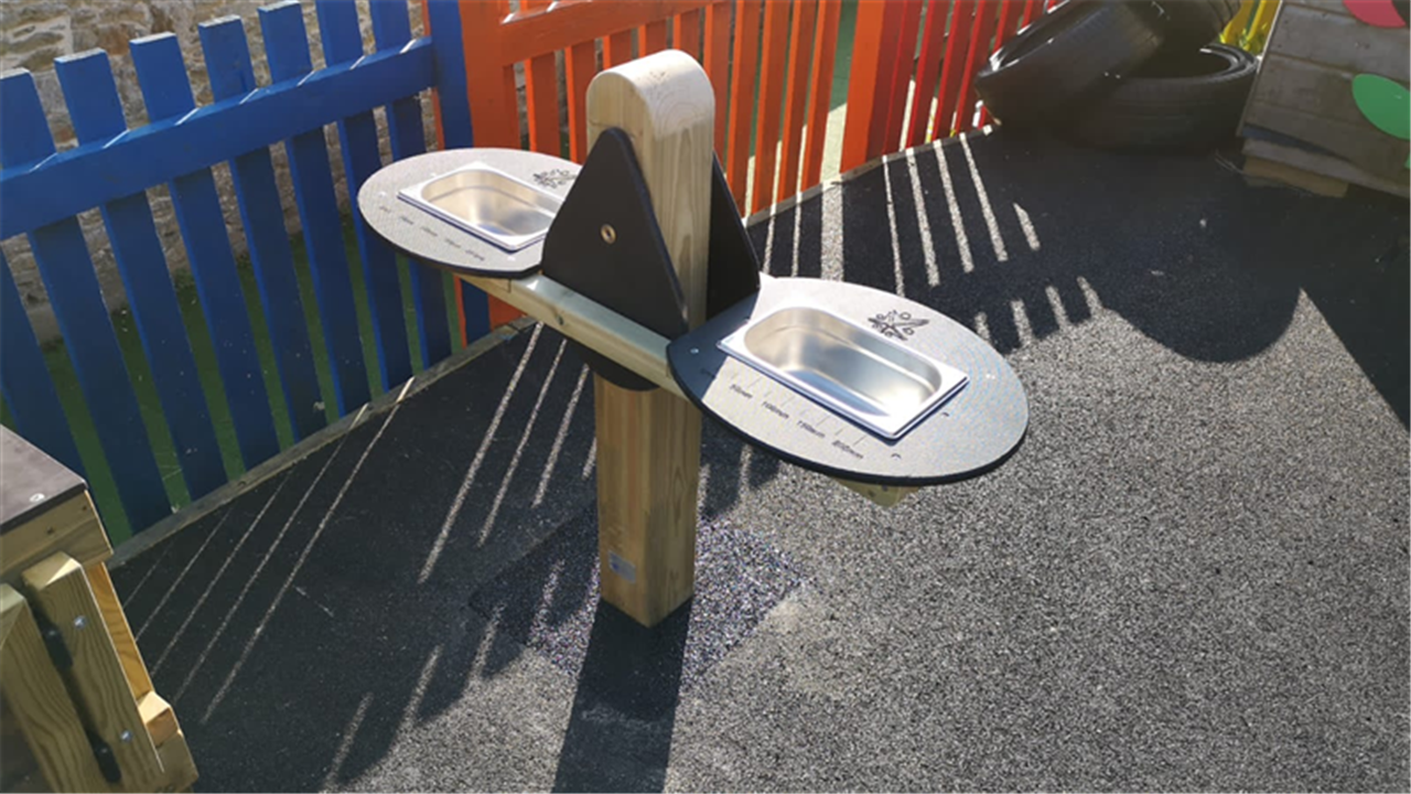 A weighing scale created by Pentagon Play. It has been installed on a black wetpour playground.