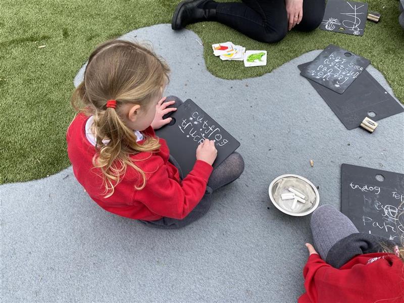 children sit with scribble boards on their knee and write with chalk