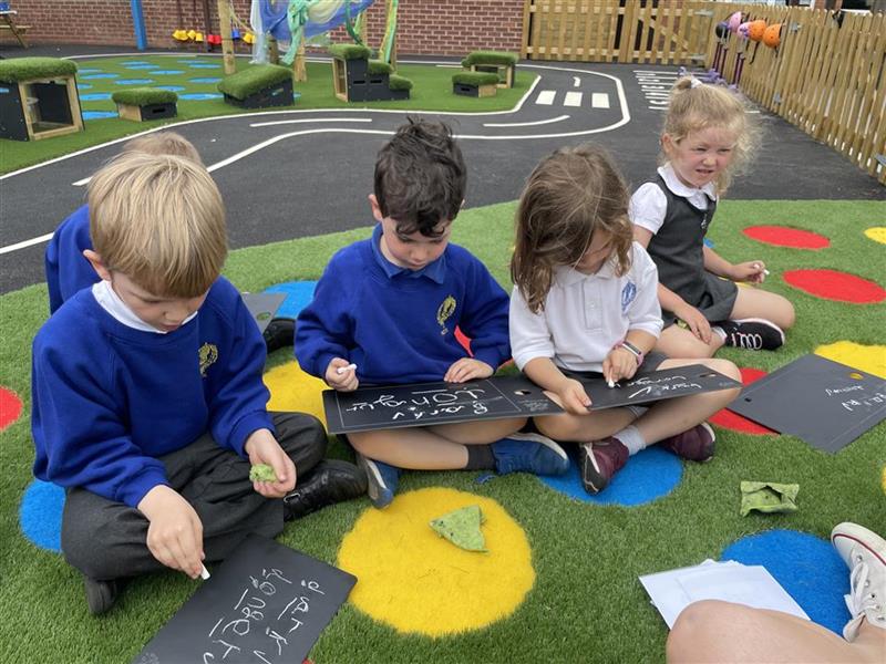 children sit on the artificial grass surfacing and draw on the scribble board