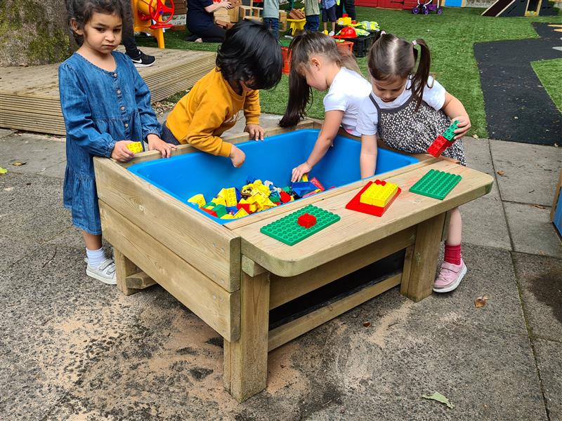 children gather around a construction table with lid and play with toys