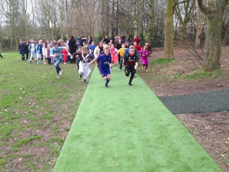 A class of children in sports kit race along the artificial grass playturf daily mile track to compete to win