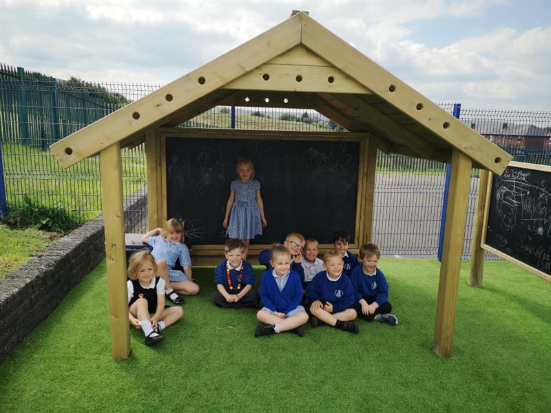 children sit gathered underneath the giant playhouse with chalkboard 