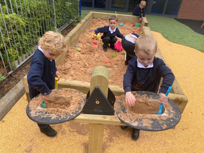 2 children playing on the weighing scales, there are 2 boys playing in the sandbox behind