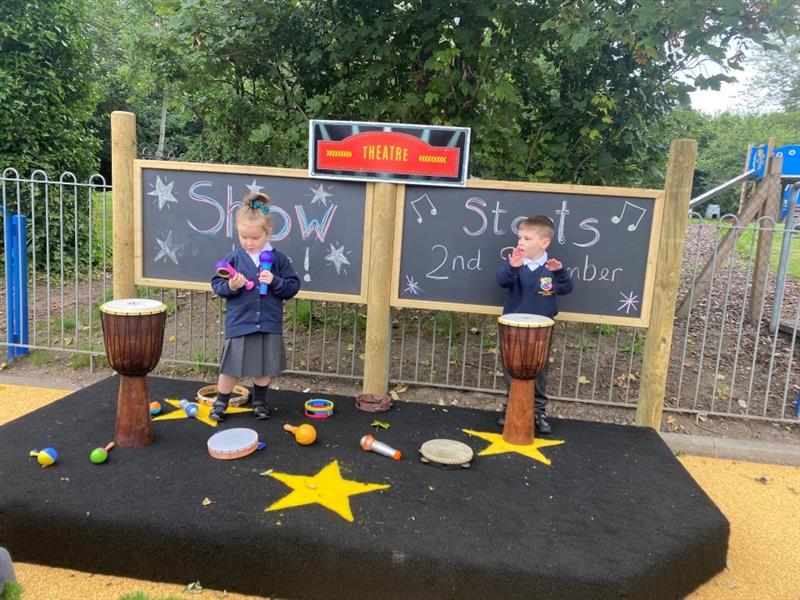 two children stand behind a pair of drums on a performance stage and play tunes