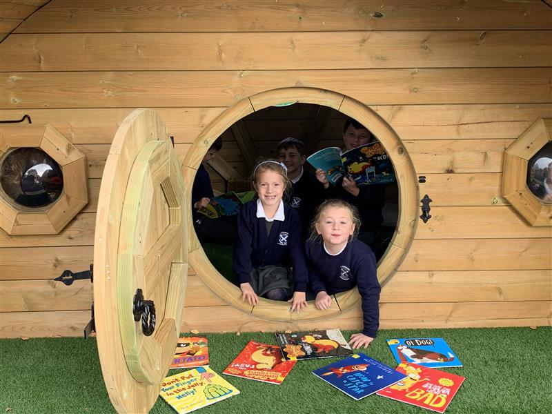 two children peek out of the hobbit house and lean on the books on the floor in front of them