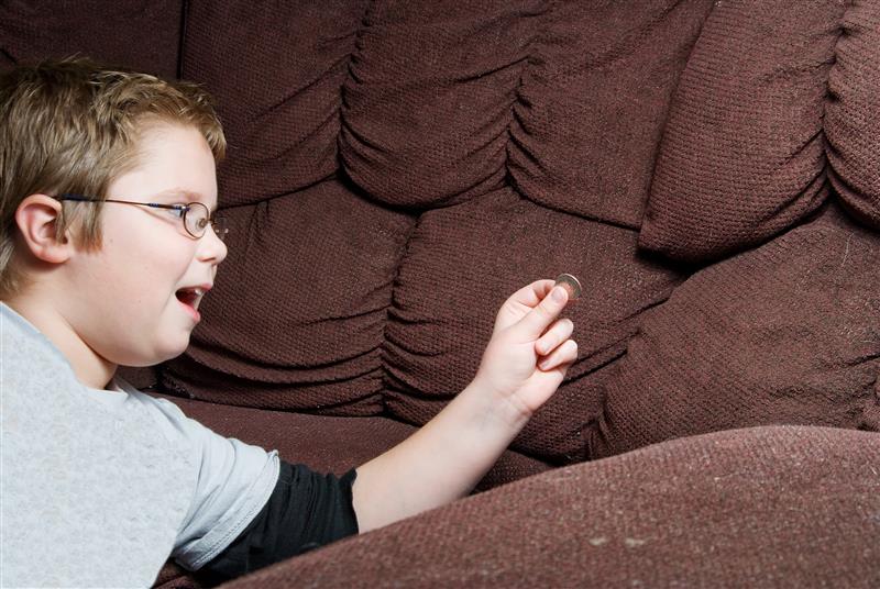 a little boy in a black and grey long sleeved top finds a coin in a brown sofa down the cushions