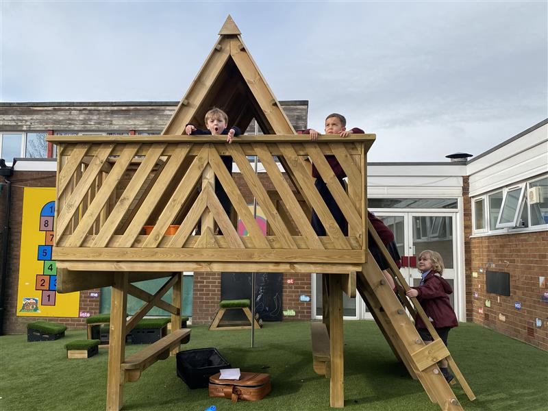 children stand on the top of the learning den and look down at the ground below