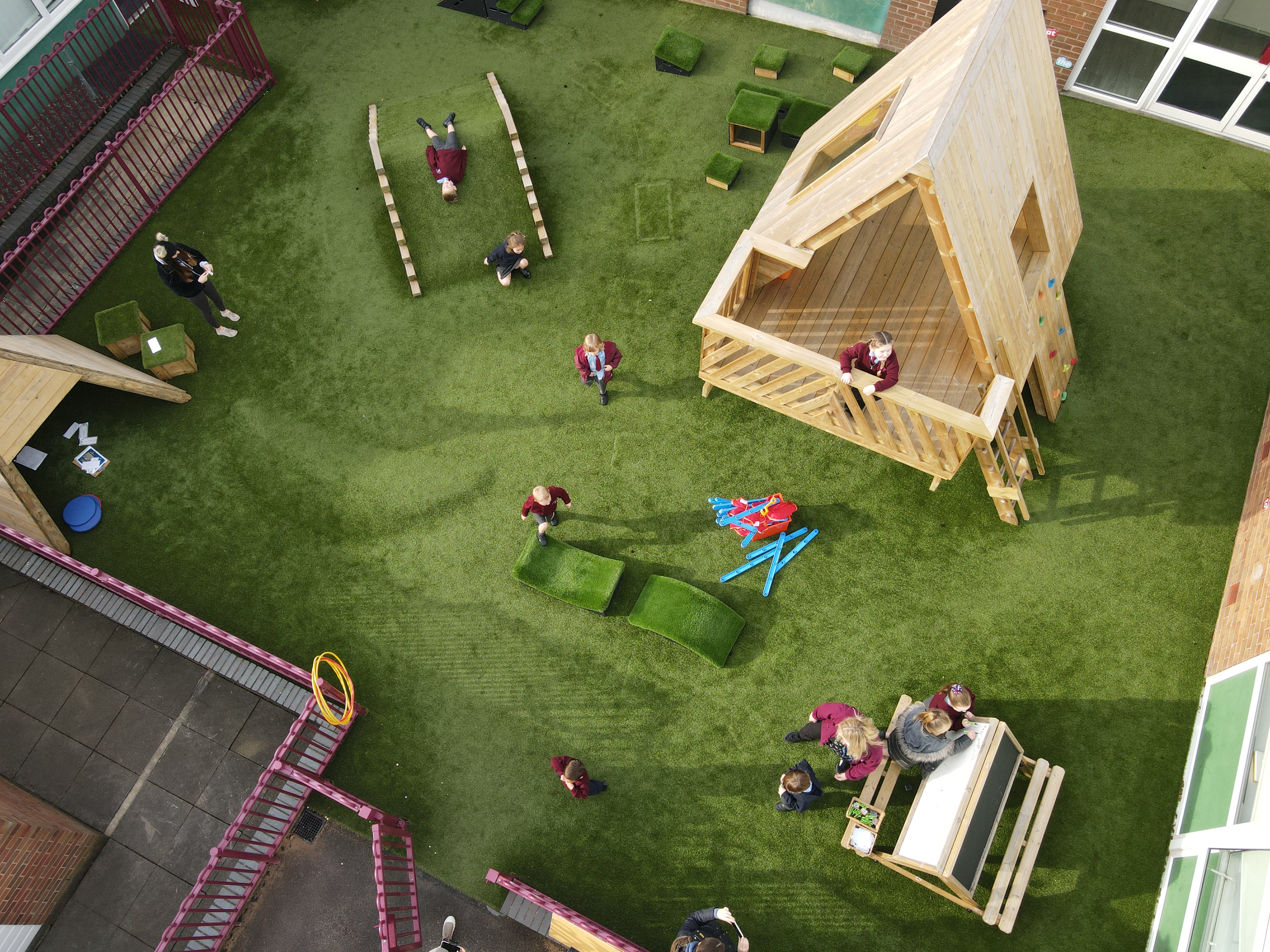 An artificial grass playground with different pieces of playground equipment and structures present.