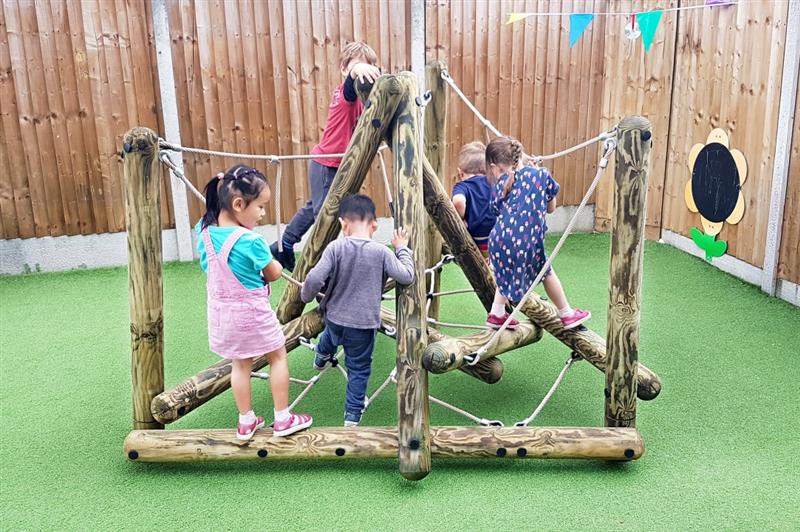 children in nursery climb on the timber climbing frame with artificial grass surfacing below
