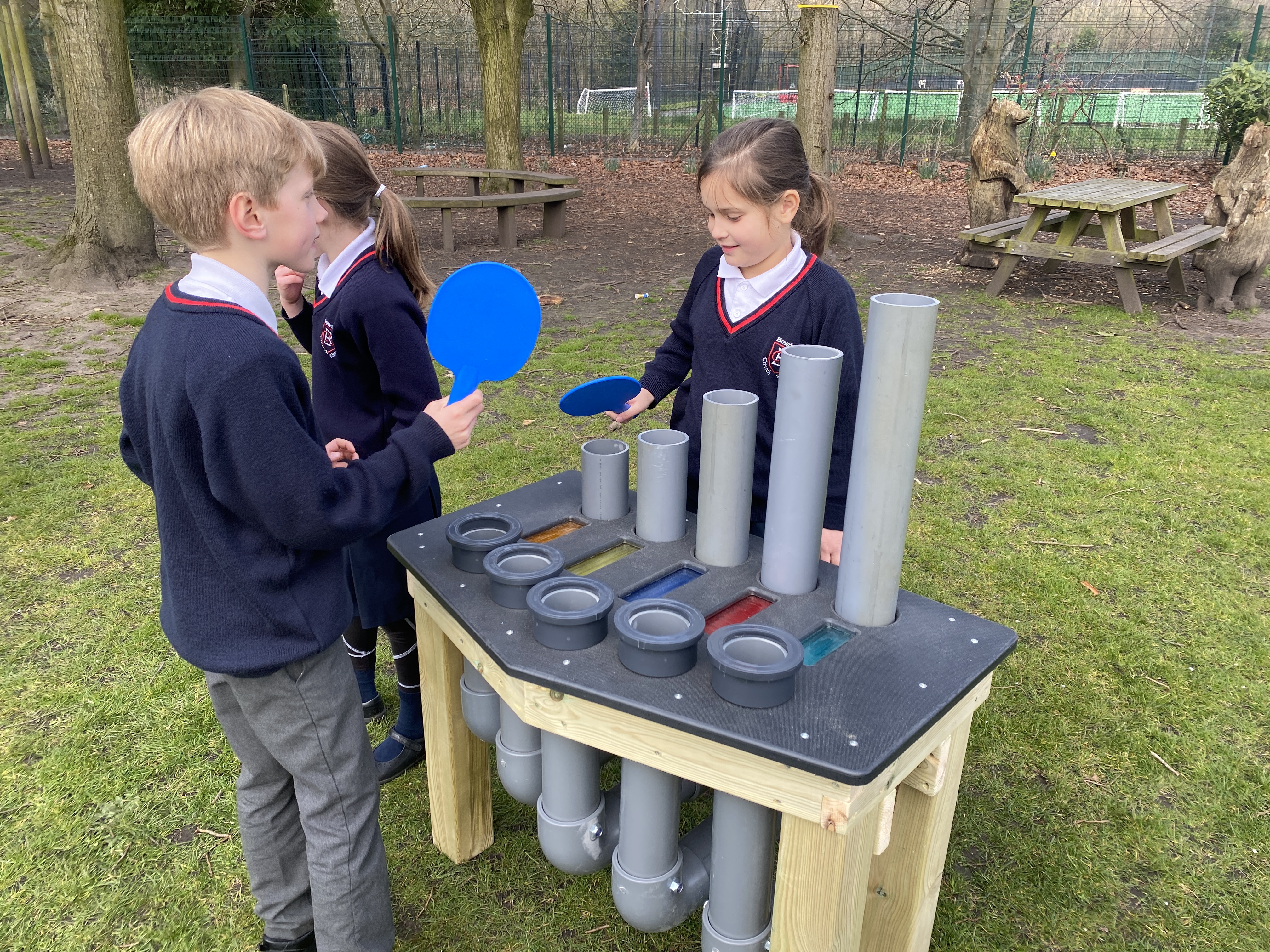 Three children are playing with the freestanding batonka, with two of the children holding plastic paddles.