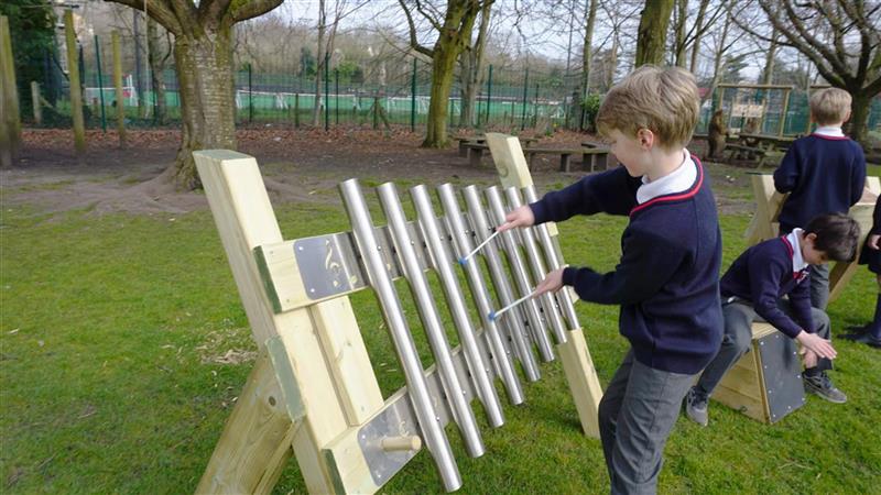 a child stands at the freestanding chimes and beats it with the two beaters