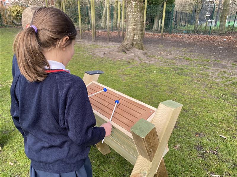 a child stands at the timber tongue drum and beats a melody out using the plastic beaters