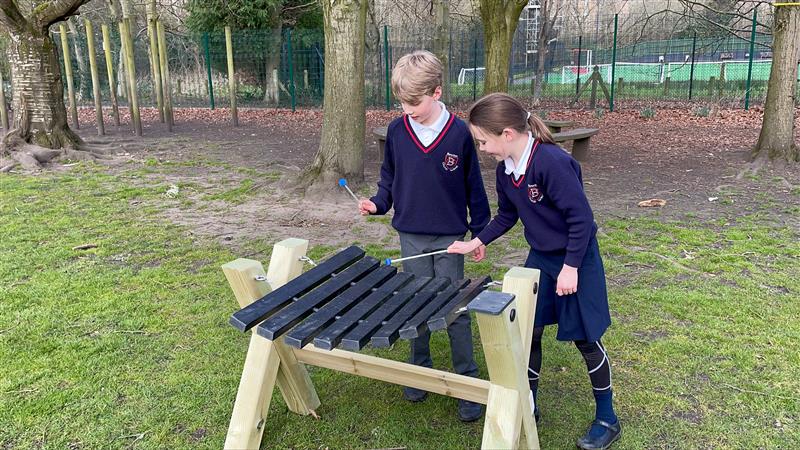 two children in navy school uniform stand and play the xylophone with the plastic beaters