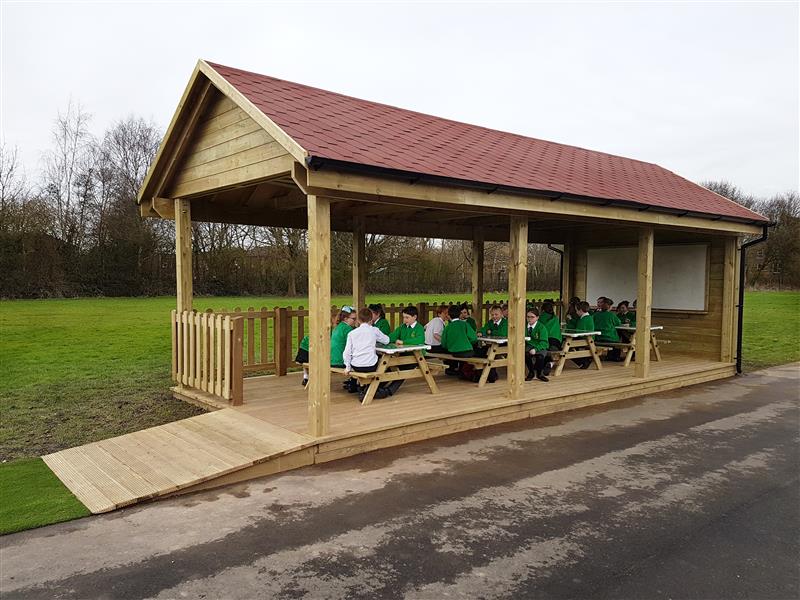 an outdoor classroom with children sat inside on the picnic tables