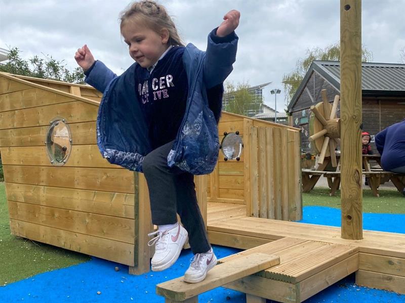 a little girl jumps down from the plank on the wooden play ship
