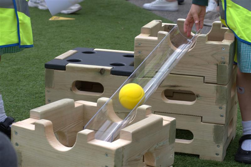  A ball rolling down the pipe of the construction blocks, a young child is pushing it down the half tube