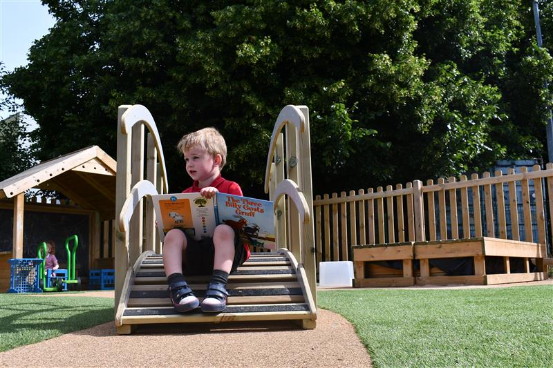 A young boy reading billy goats gruff on the play bridge in his playground