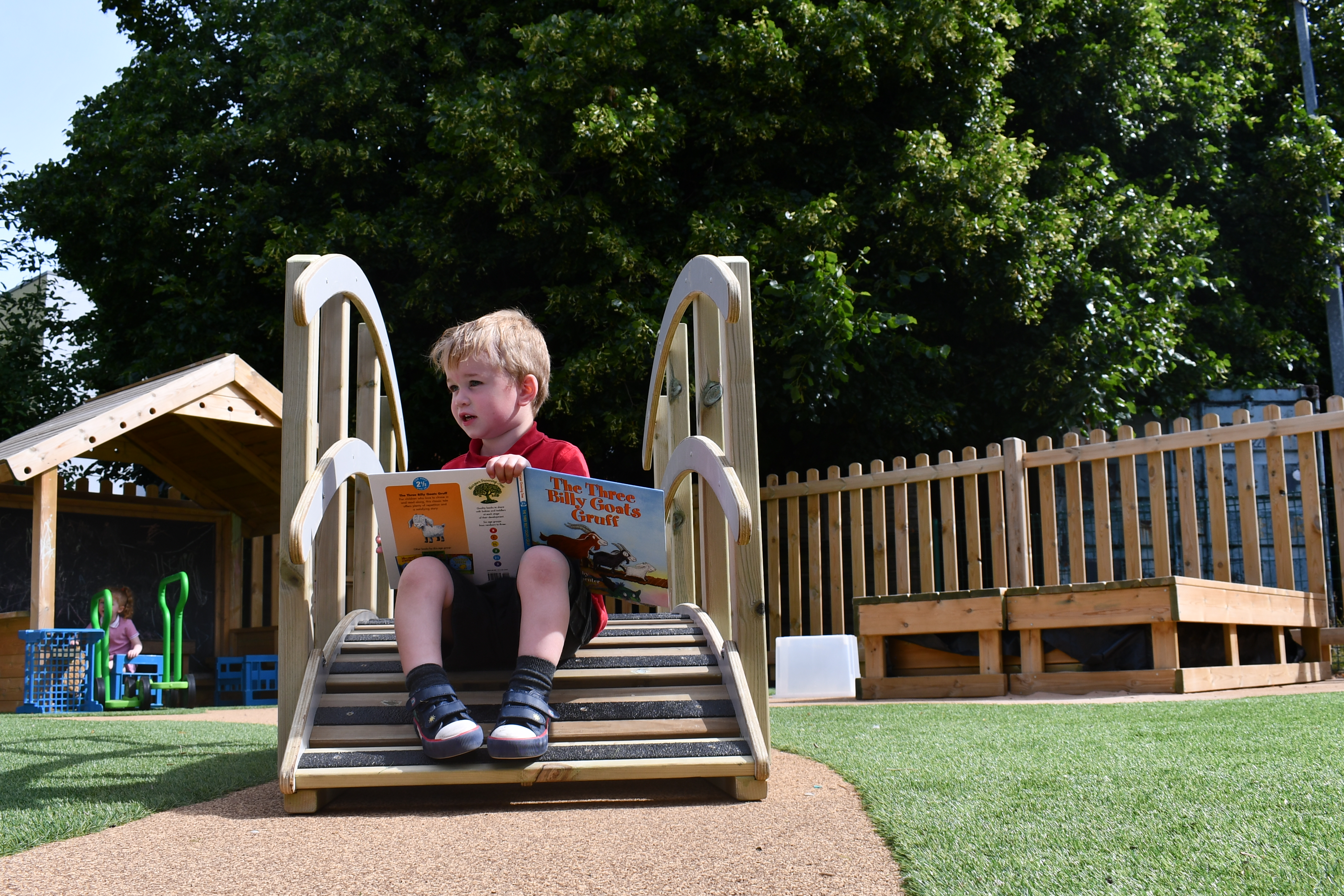 A little boy is sat on the Play Bridge with Handrails and is reading "The Three Billy Goats Gruff".