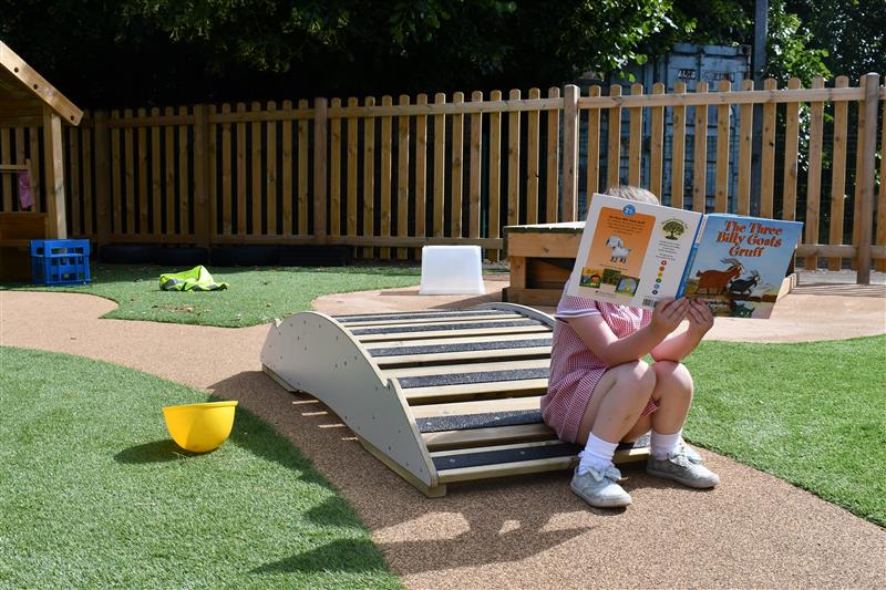 a child sits on the end of the playbridge walkway and reads a storybook
