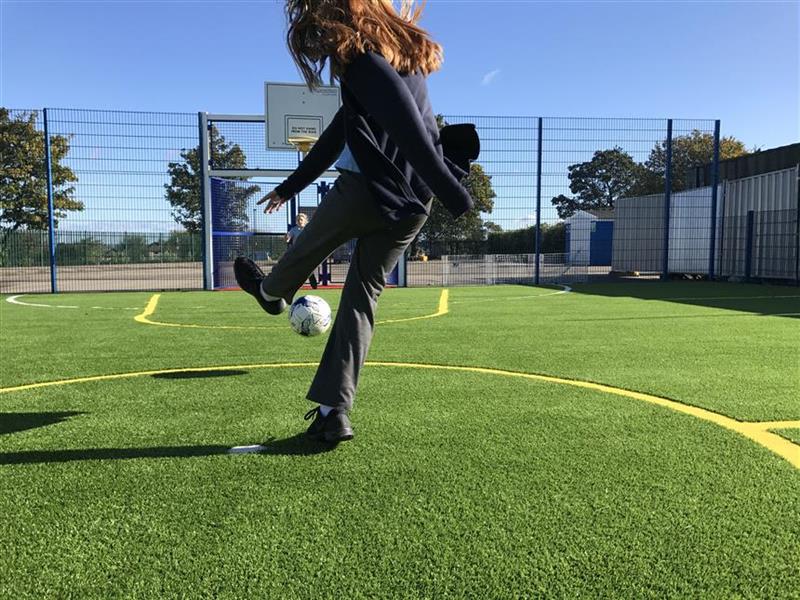 A young girl kicking the ball into the net of the muga pitch