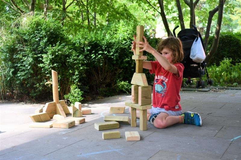 a little boy sits on the floor and creates a tower with wooden blocks that come in the wooden construction skip