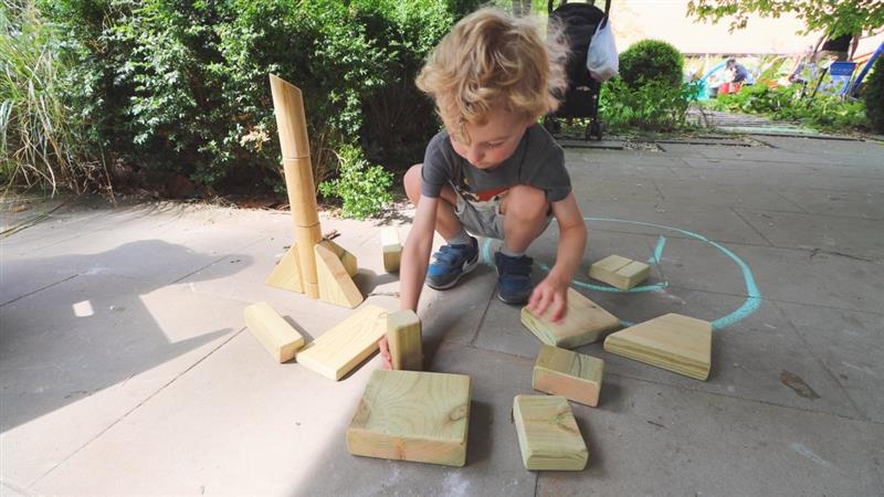 a little boy stands on the floor and lays out the wooden blocks in front of him as he arranges them