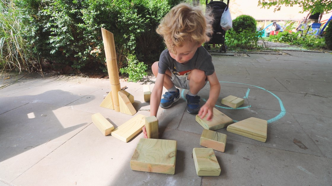 A little boy is playing with a set of wooden blocks and is starting to build a tower from them.