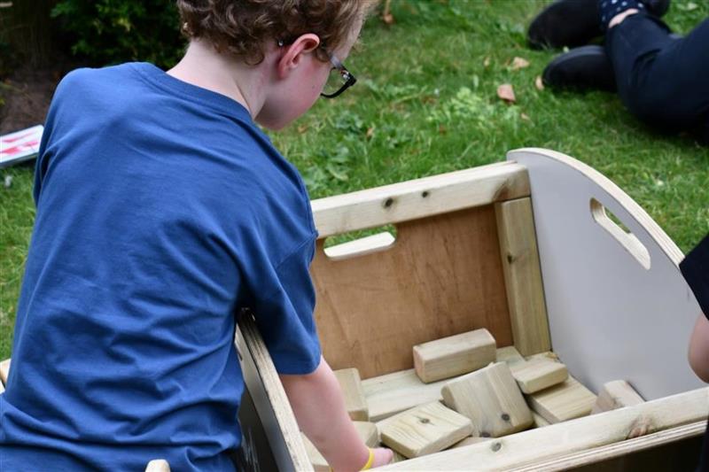 a child stands by the mini skip and puts his arm in to grab wooden blocks
