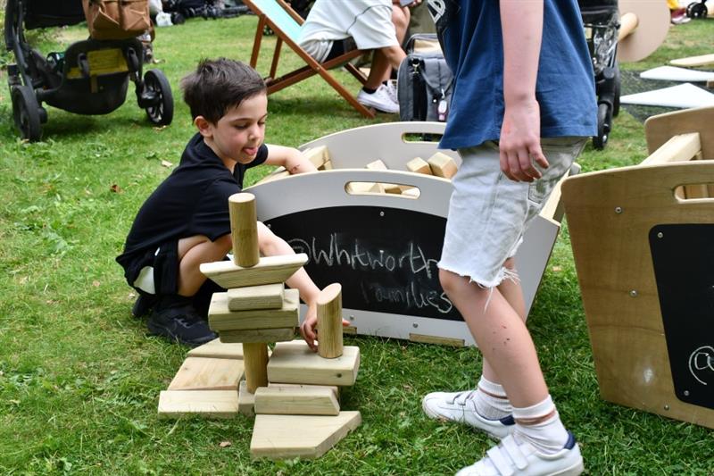 a little boy sits on the grass and takes blocks out of the skip and stacks them into a tower
