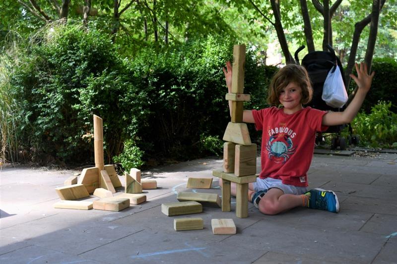 a little boy sits on the floor and builds a tower with wooden blocks from the mini skip