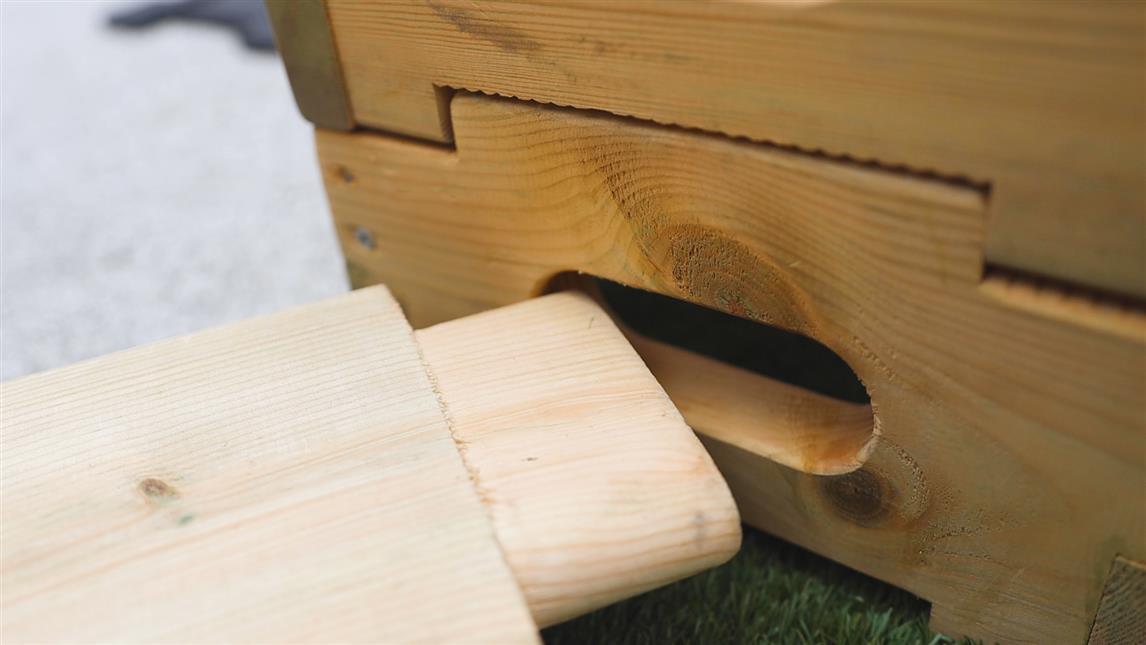 A close up shot of a wooden Accoya plank being connected to a hole in the side of a wooden box.