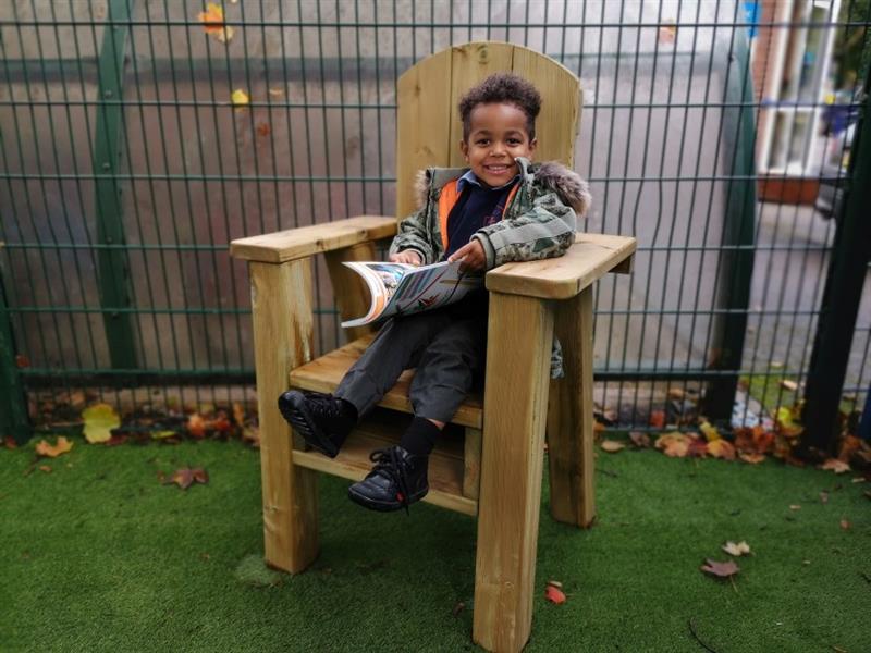 a little boy sits in the storytelling chair and smiles at the camera as he holds a book