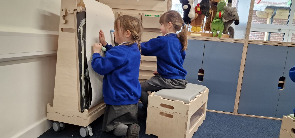 Two children are drawing on a piece of A3 paper, which has been attached to a movable whiteboard.