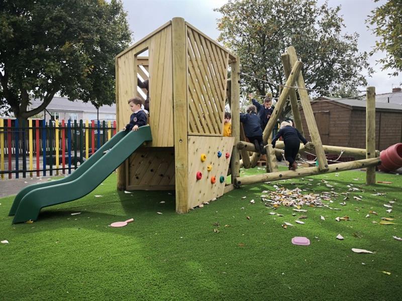 children run around on the timber climber with green slide and climbing wall