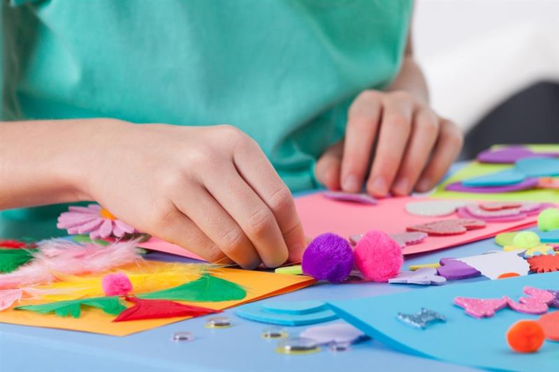 a child sits and makes something with pom poms and glue