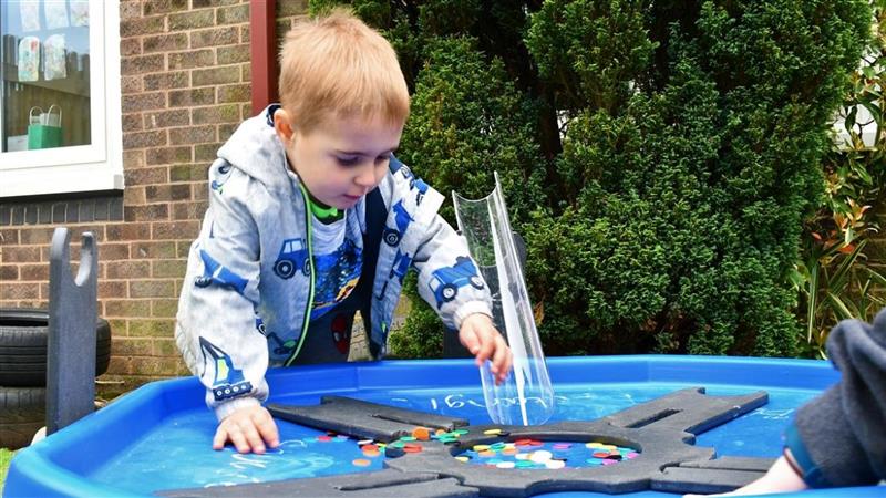 a little boy stands over the blue tuff spot table and plays with counters
