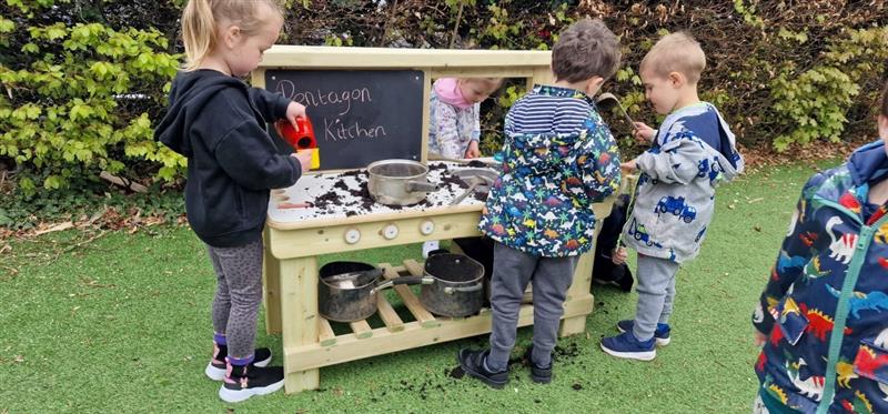 children build their social skills as they all stand around the  mud kitchen and talk with one another 